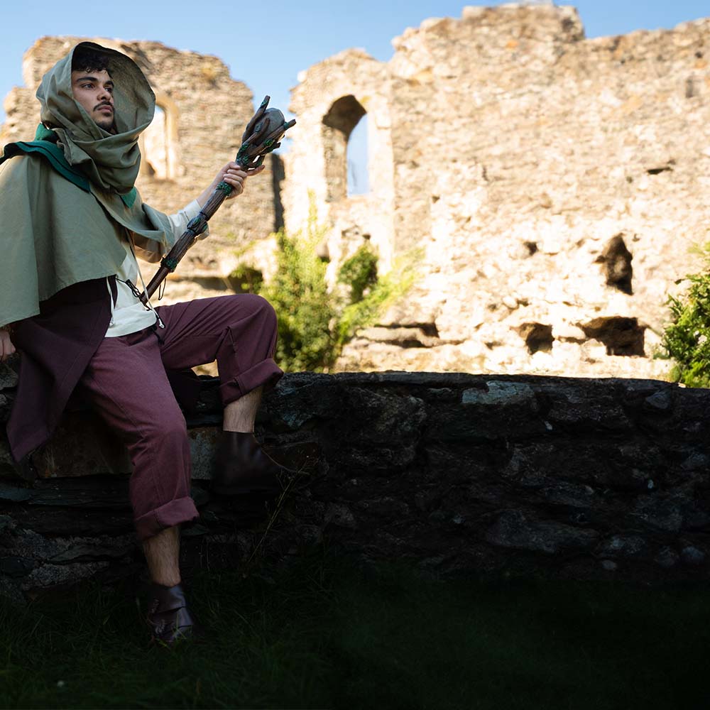 D&D druid, dressed in garments made by Brugschneider, is sitting on a old wall waiting for his party.