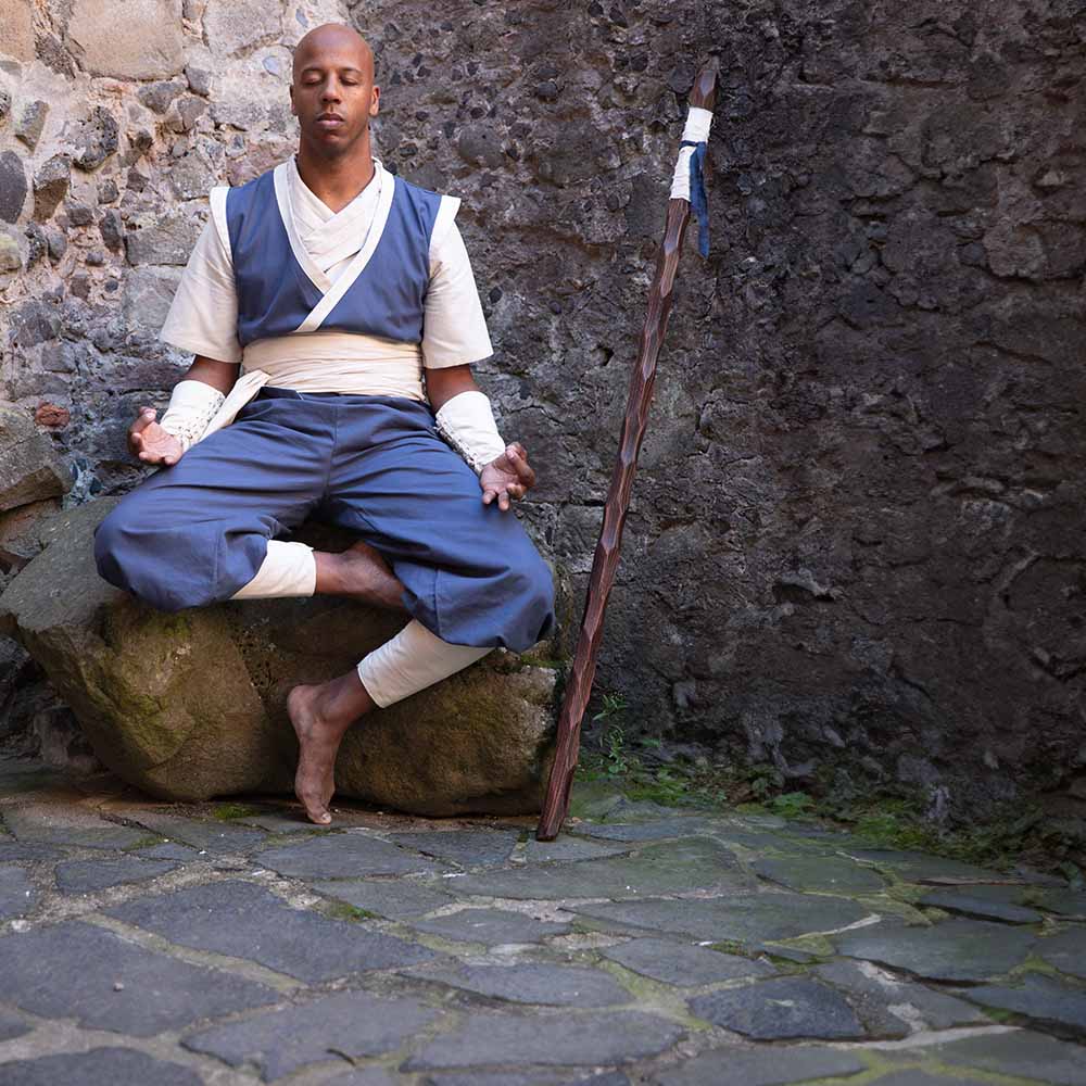 D&D monk, dressed in the blue garments from Burgschneider, is meditating on a giant rock.